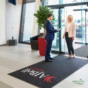 Tapete de entrada personalizado com logótipo aplicado à entrada de uma receção, com duas pessoas em conversa