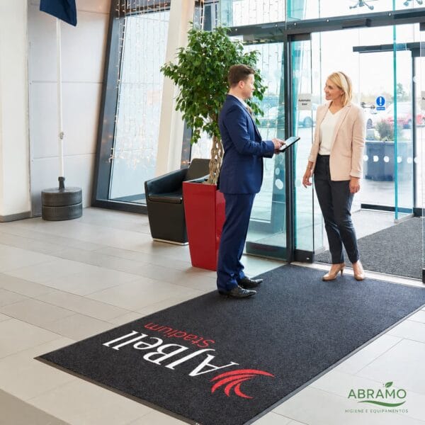 Tapete de entrada personalizado com logótipo aplicado à entrada de uma receção, com duas pessoas em conversa