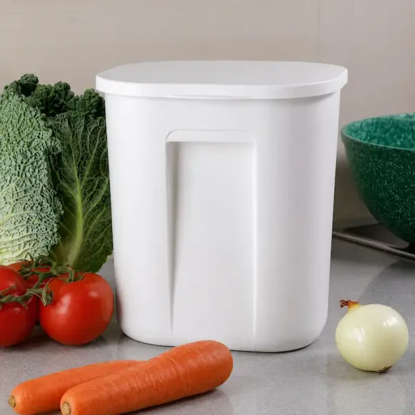 Balde do lixo com tampa branco numa bancada de cozinha, rodeado de legumes